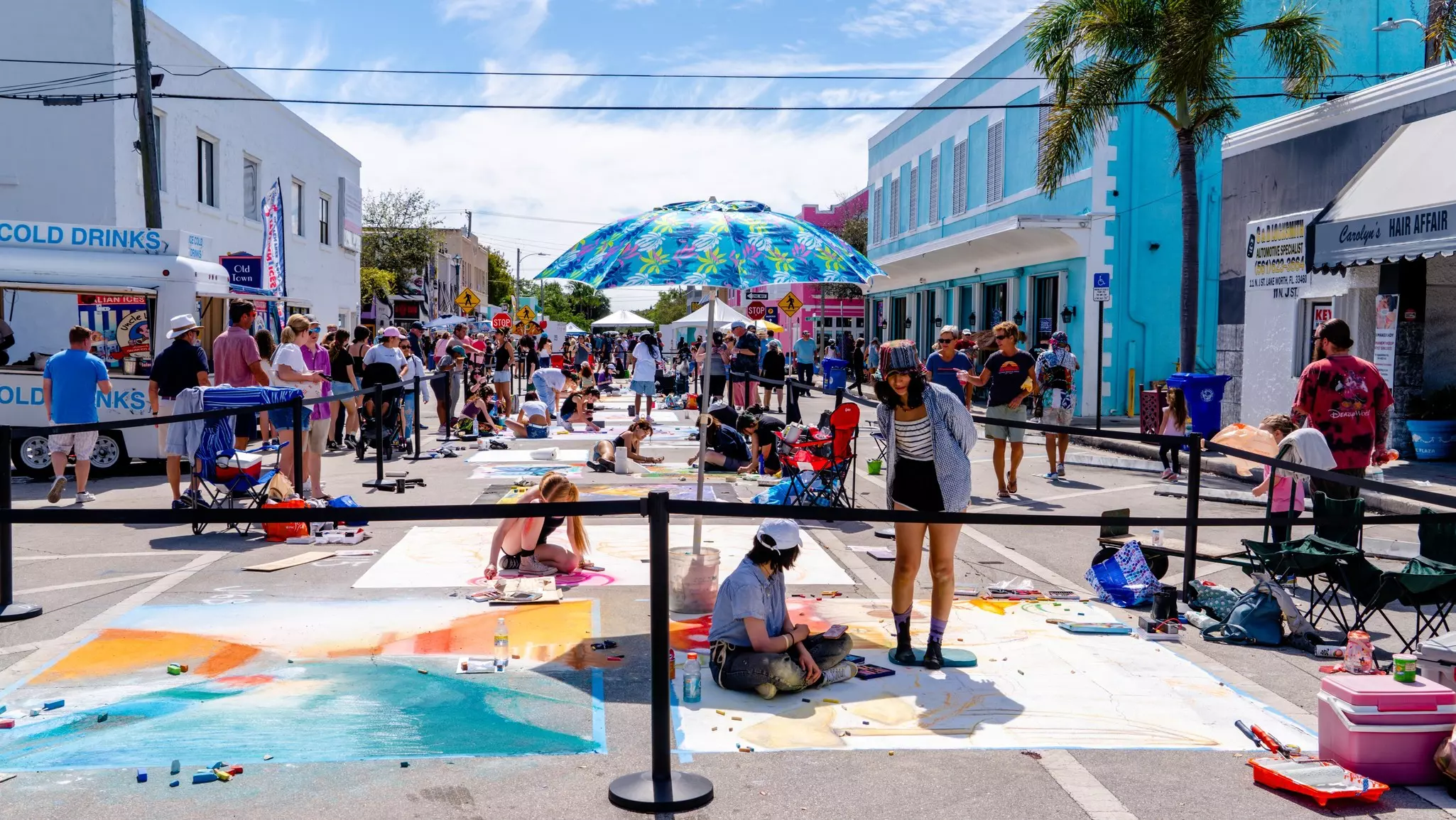 People are seen painting murals on the sidewalk on a beachside boulevard.
