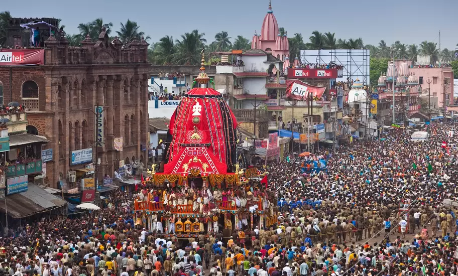 Huge red-canopied festival chariot surrounded by dense crowds on Puri's Grand Road during Rath Yatra, police lines at right