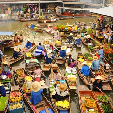 A vast amounts of small wooden boats gather to trade goods at  Amphawa floating market. Most of the boats sell food, specifically fruits. Tourist wielding cameras watch on.