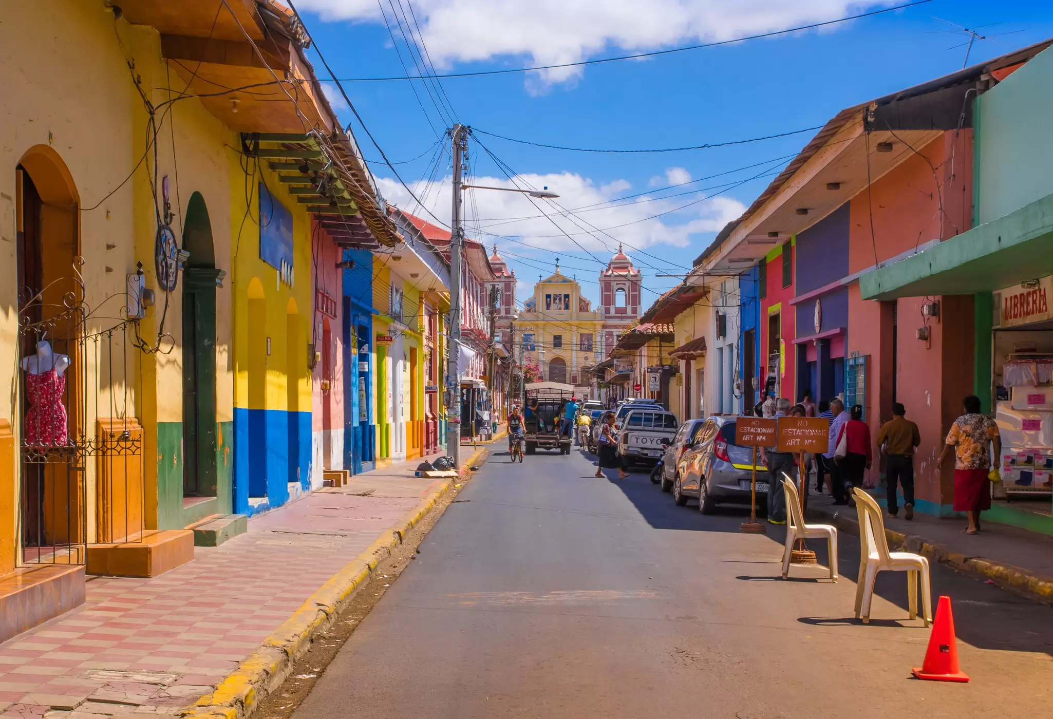 Brightly colored one-storey houses along a narrow street with a church at the end.