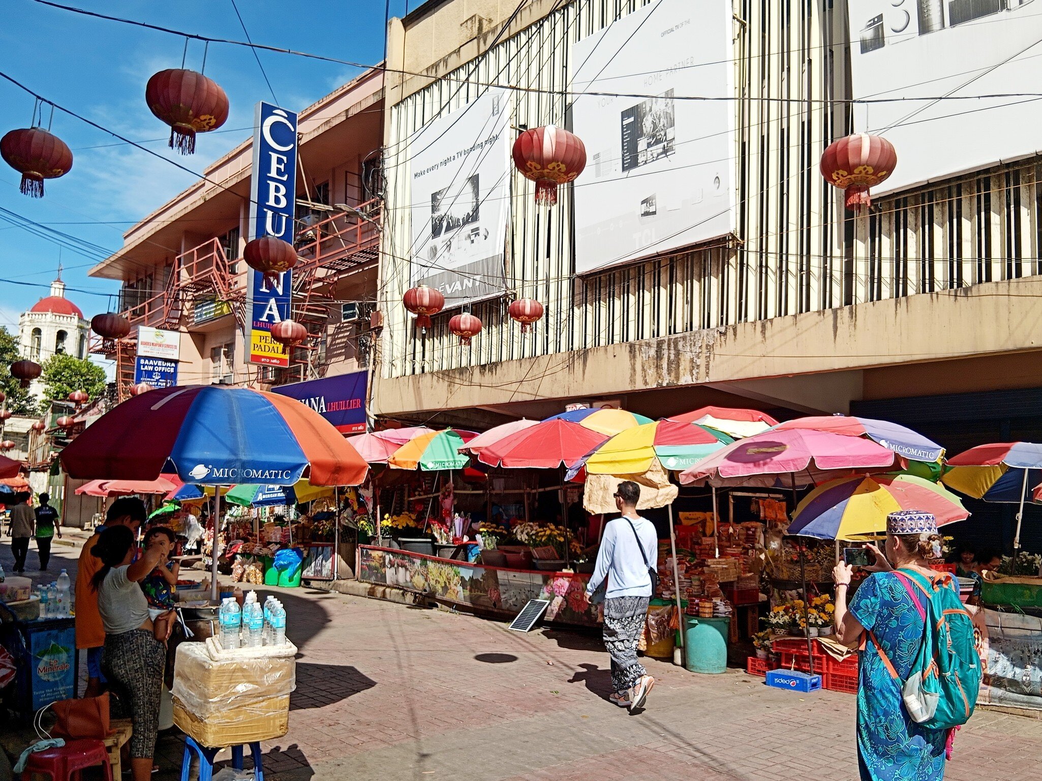 Market stalls under rainbow umbrellas and red lanterns on a street in Cebu City, Philippines; sign reads CEBUANA