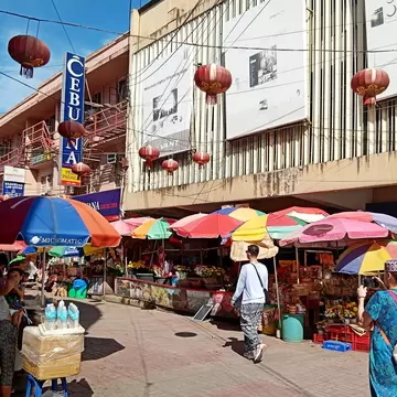 Market stalls under rainbow umbrellas and red lanterns on a street in Cebu City, Philippines; sign reads CEBUANA