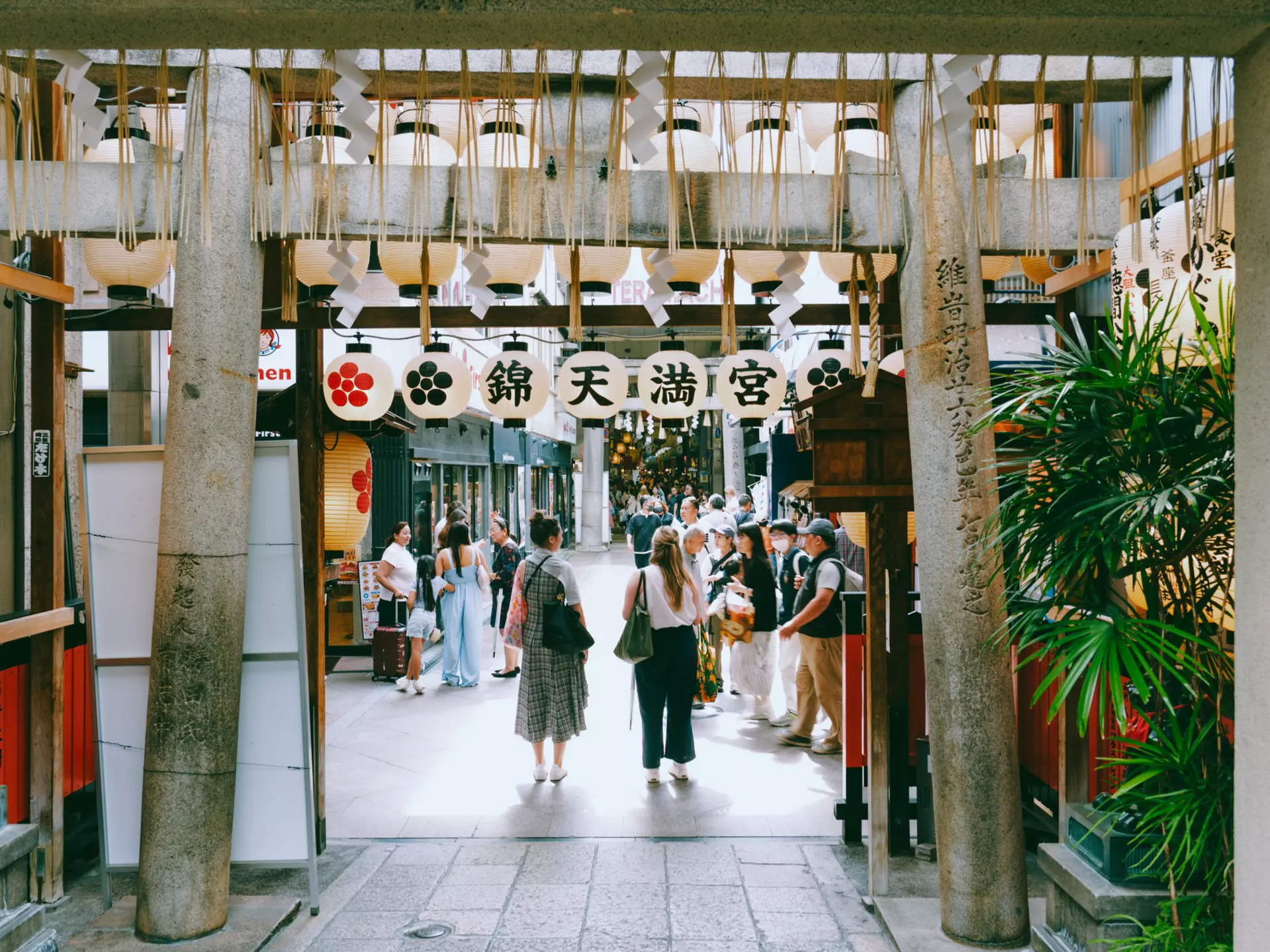 Women walk through Kyoto's vibrant Nishiki Market beside dangling lanterns. 
