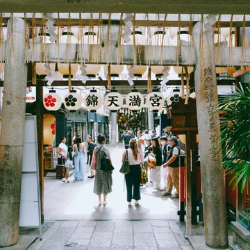 Women walk through Kyoto's vibrant Nishiki Market beside dangling lanterns. 