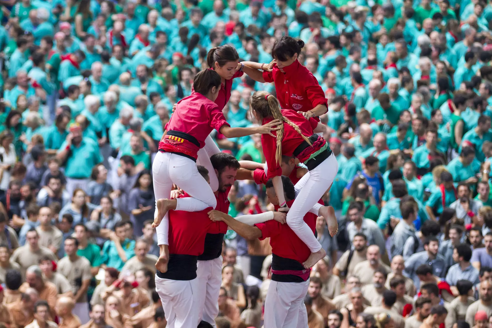 People climbing on top of each other in formation to form a tower of humans. A large crowd watches on.