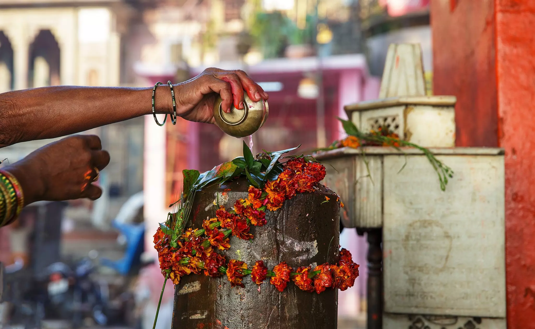 A hand pouring a golden cup over an object with a flower garland.