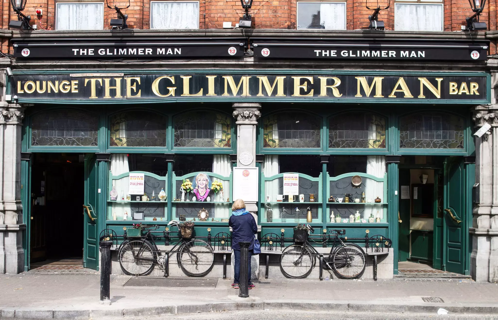 A woman stands facing the facade of an old pub called The Glimmer Man