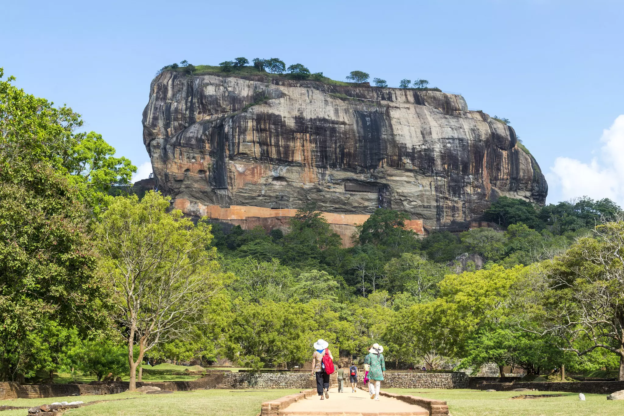 Visitors walk through gardens towards a vast rocky outcrop.