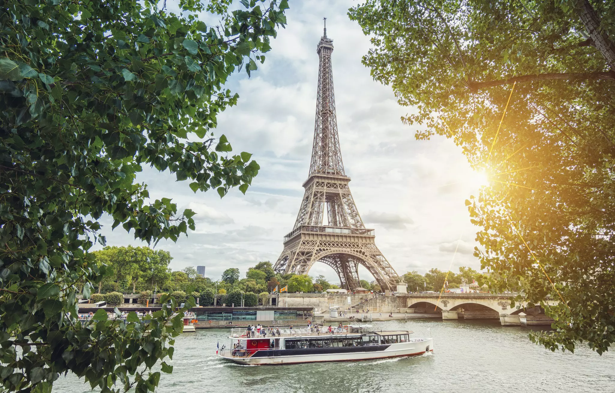 View from the Seine shore to the Eiffel Tower in Paris, with a cruise boat in front.