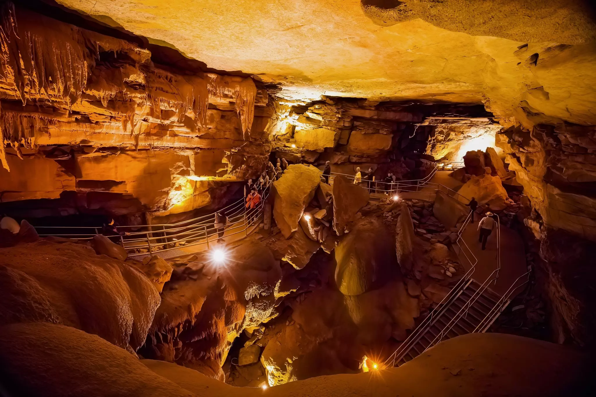 Tourists following marked paths within a massive cavern with stalactites and stalagmites.