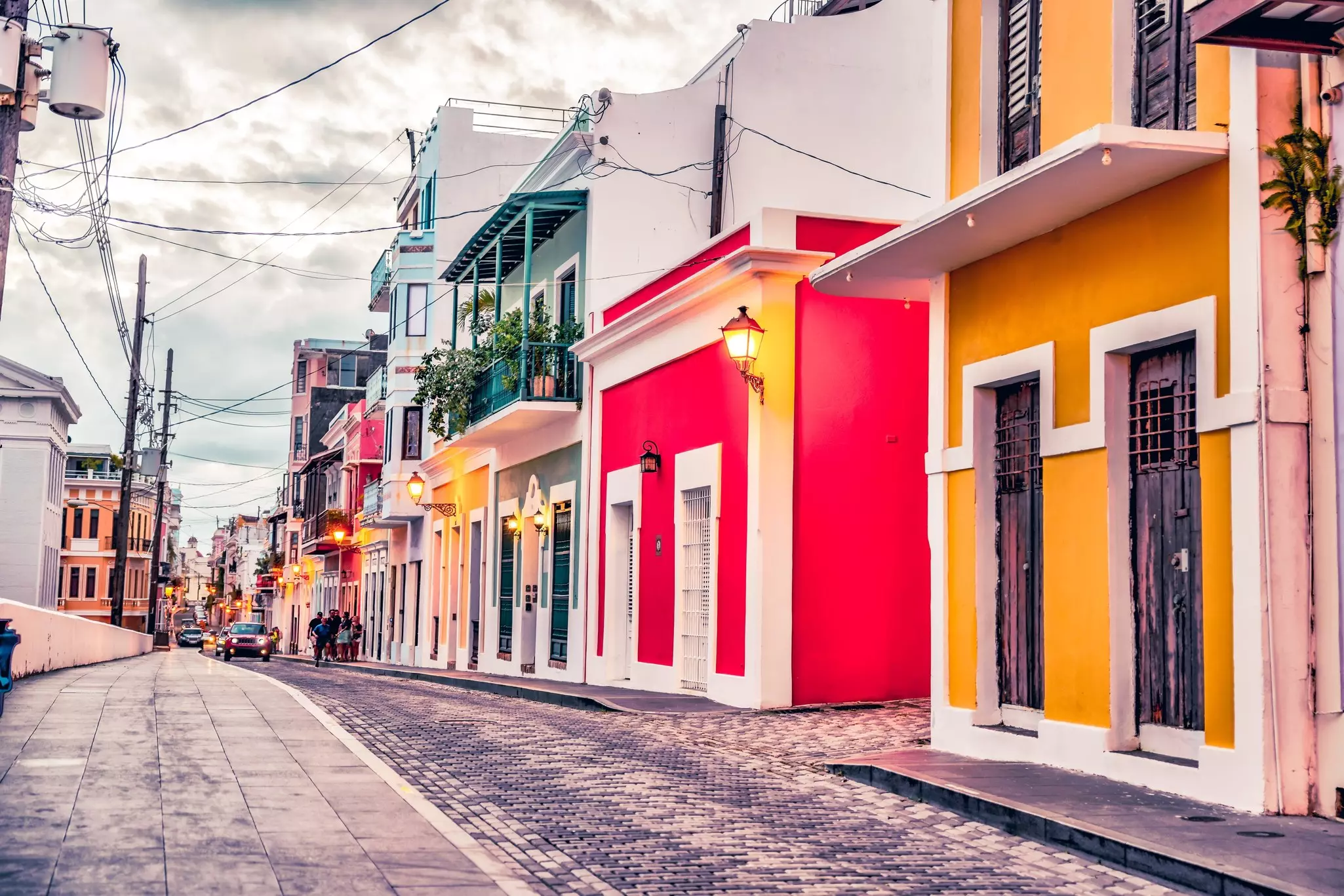 Brightly painted houses line a cobbled street in a city, with a cloudy sky overheard.