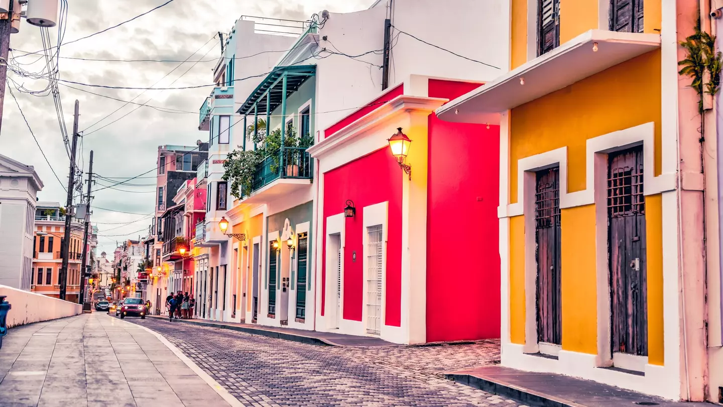 Colorful houses of yellow, red, green, and white line a cobblestone street on an overcast day.