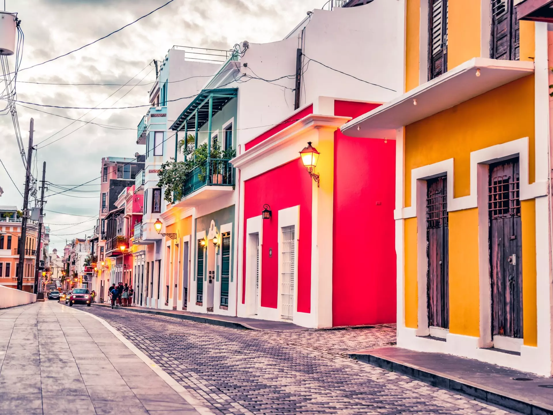 Colorful houses of yellow, red, green, and white line a cobblestone street on an overcast day.