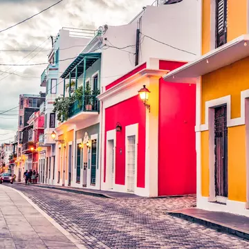 Colorful houses of yellow, red, green, and white line a cobblestone street on an overcast day.