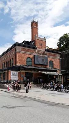A redbrick building with people standing in front and sitting in an outdoor cafe.