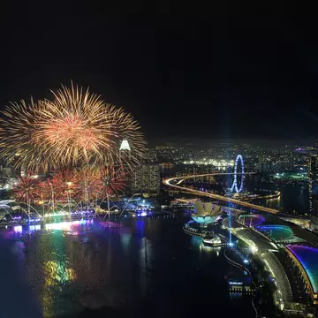 An aerial view of the Singapore NYE firework display. With a series of bright fireworks lighting up the sky above the city's skyscrapers.