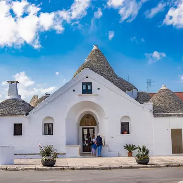 Whitewashed Trullo Sovrano with grey conical stone roofs and arched entrance under a blue sky in Alberobello, Italy