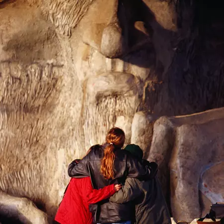 Three people facing a troll sculpture under a bridge in Seattle, Washington.