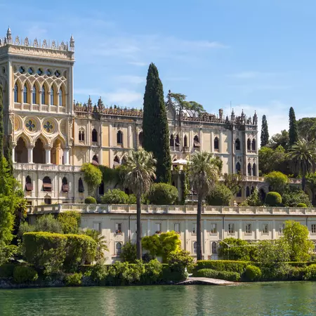 An ornate palazzo with cyprus trees in front on Lake Garda. 