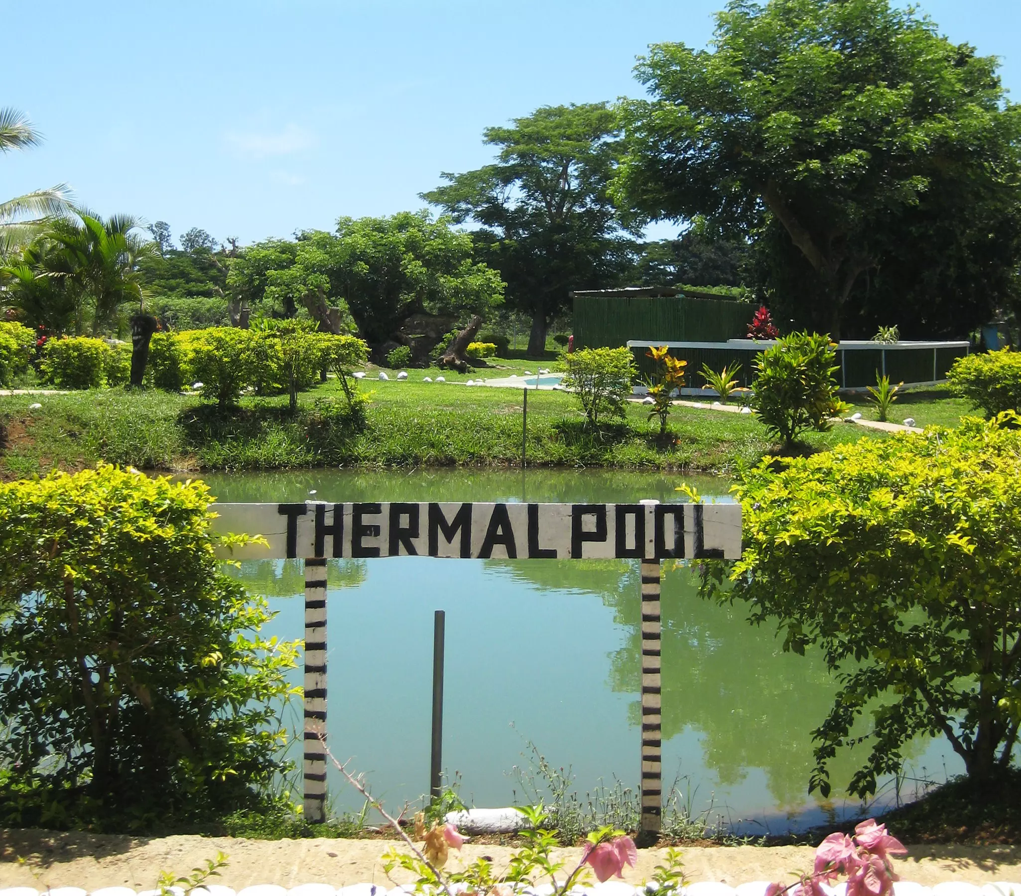 A sign announces a thermal pool amid greenery and flowers
