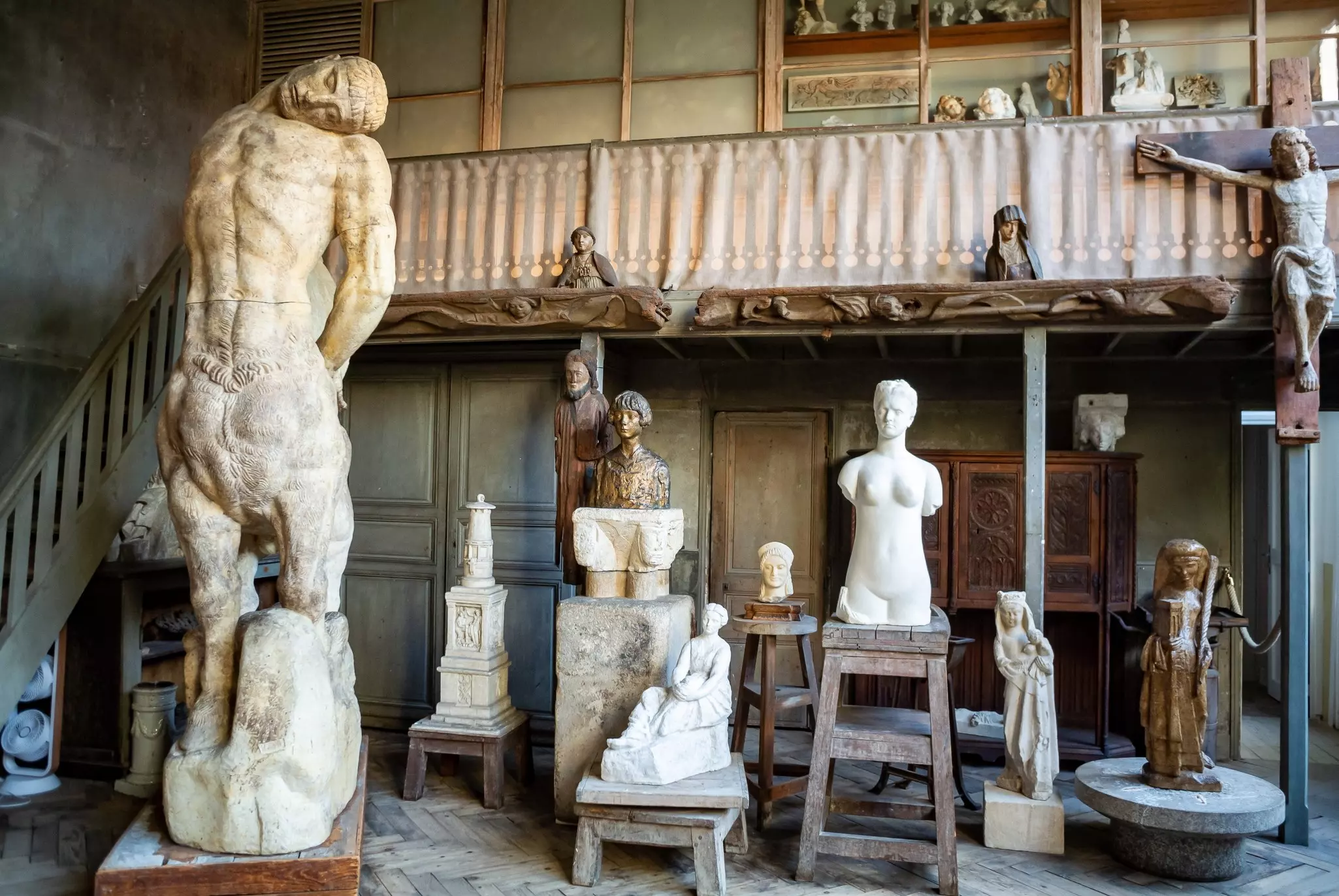 Figurative marble sculptures and wooden carvings in an artist's studio.