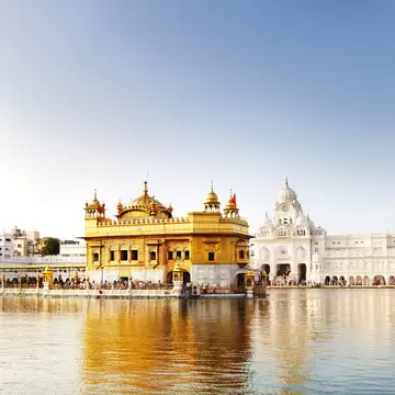 The gilded Golden Temple and white marble buildings reflected in a still pool under a clear blue sky in Amritsar.