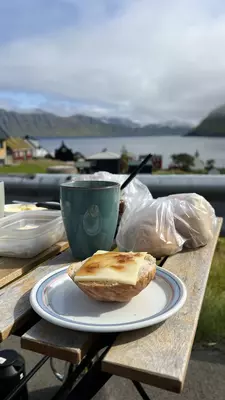 A cup of tea and a bun with cheese and jam on a small table with the ocean in the background in Oydarfhørður, Faroe Islands