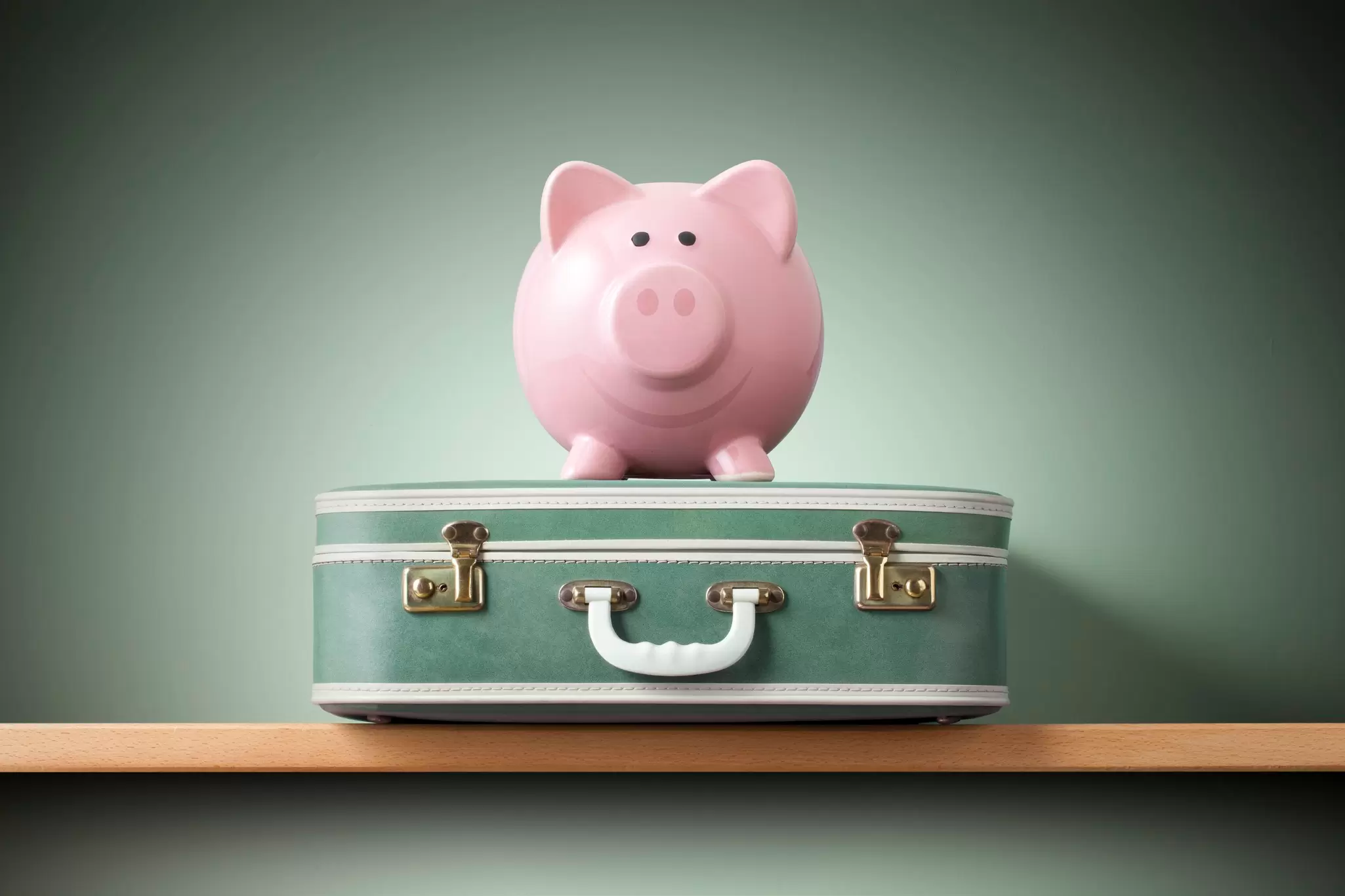 Pink piggy bank sitting atop a vintage green suitcase on a wooden shelf