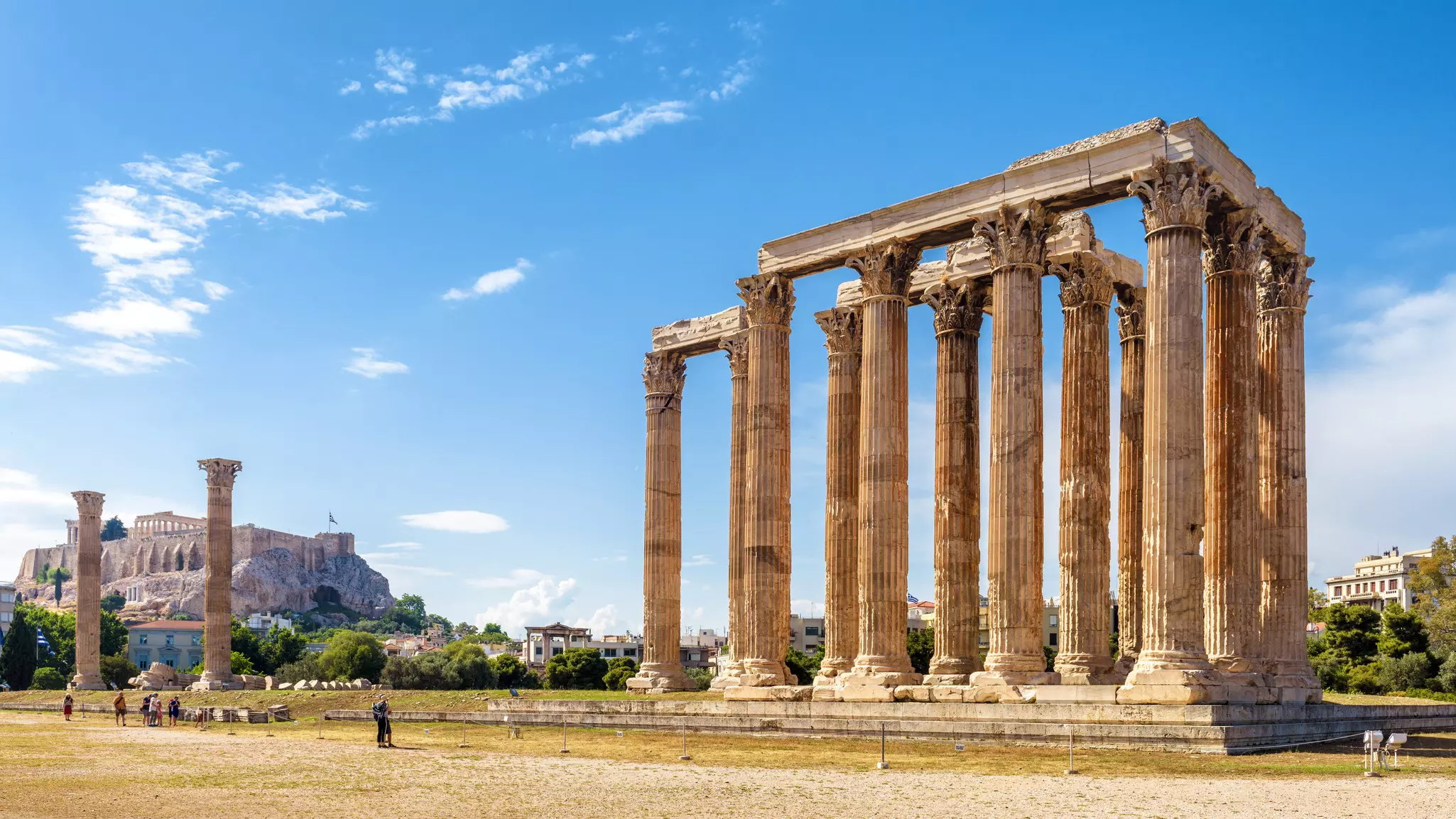 A handful of people look up at the ruins of a temple with tall columns on a sunny day.