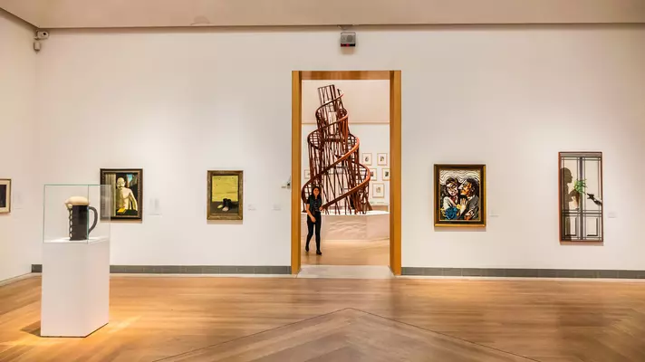 A gallery space with various pieces of modern art on the walls and a central spiral sculpture viewed through a doorway