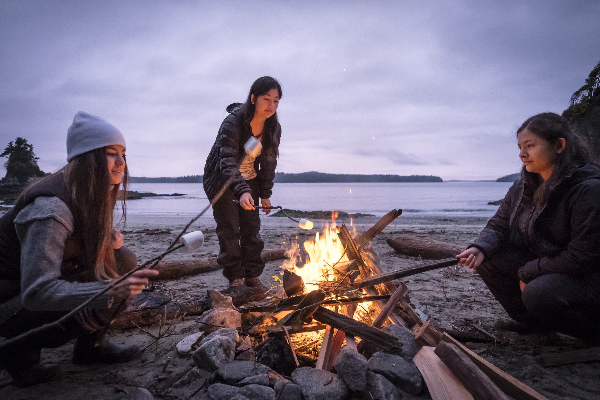 Mixed ethnic, Eurasian sisters roast marshmallows on sticks.  Bamfield, Vancouver Island, British Columbia, Canada.