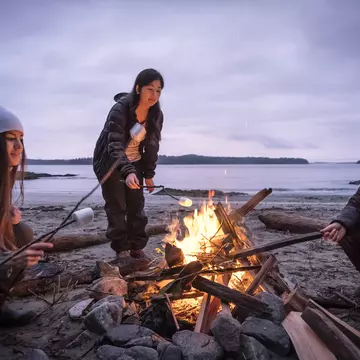 Mixed ethnic, Eurasian sisters roast marshmallows on sticks.  Bamfield, Vancouver Island, British Columbia, Canada.
