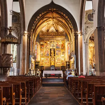 Funchal cathedral interior with wooden pews leading to a gilded Gothic altarpiece under a pointed arch