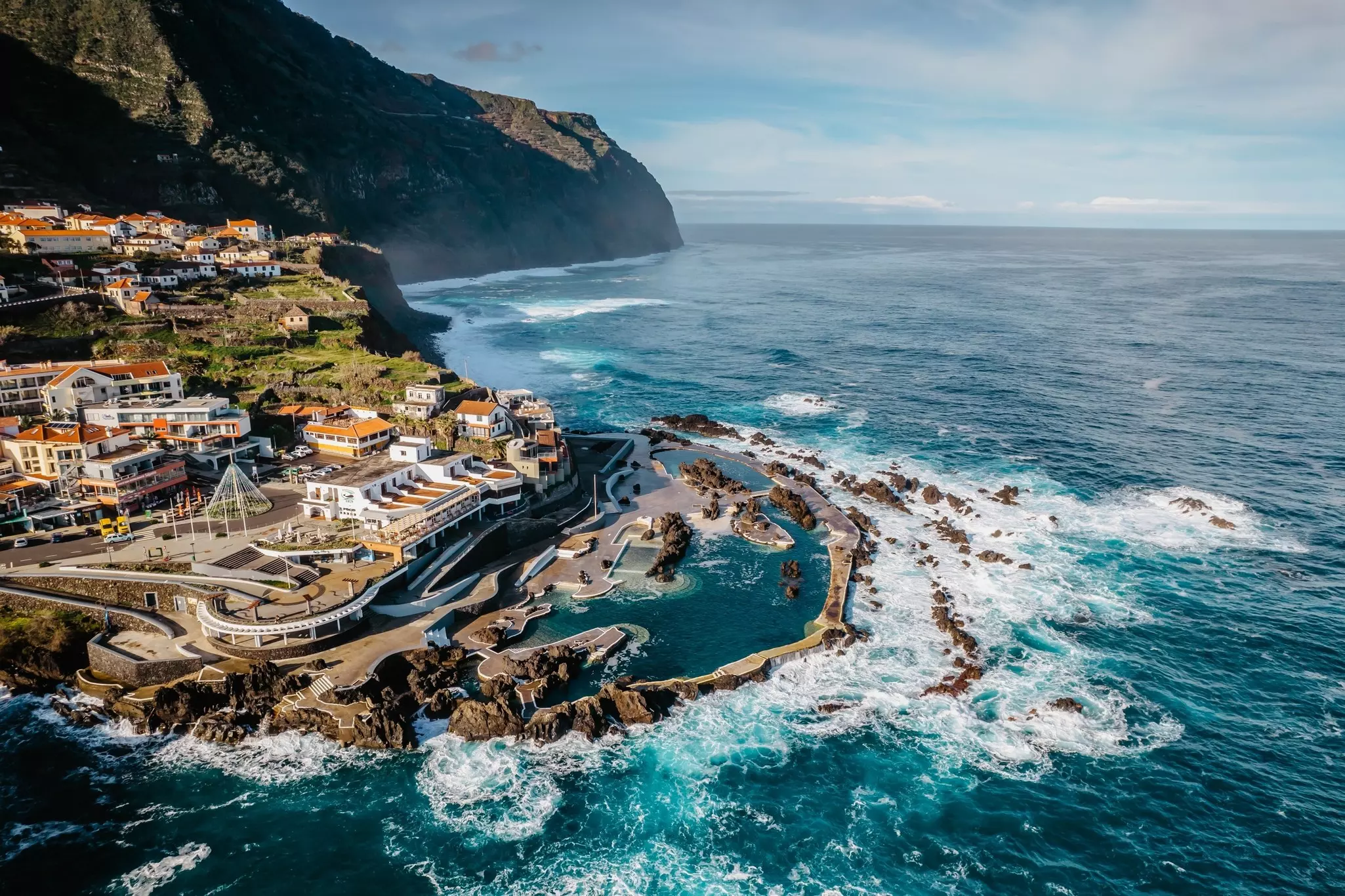A natural pool next to the ocean, with white-capped waves crashing around rocks.