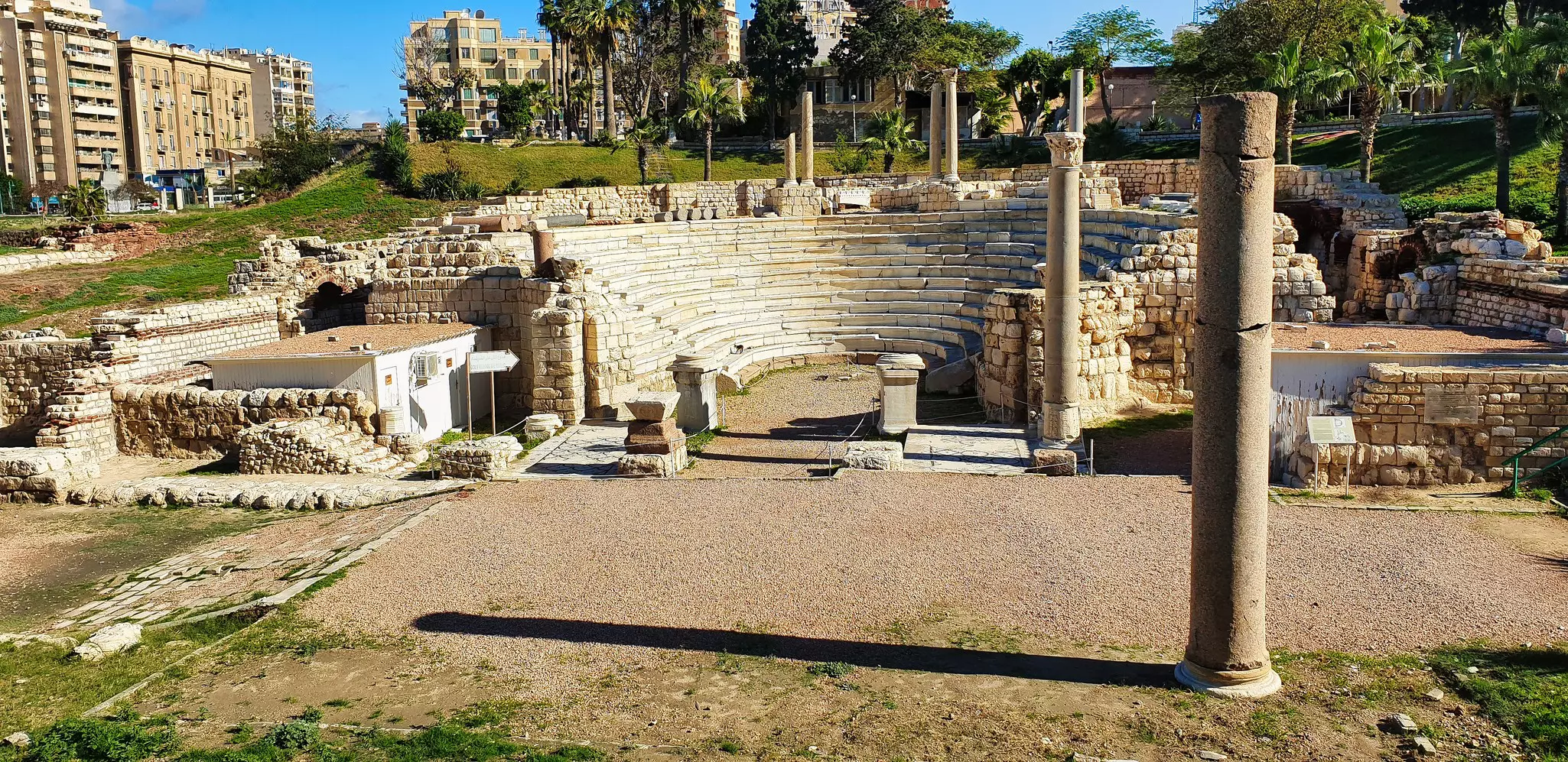A Roman amphitheater set into a hillside in a park in Egypt; several tall columns are around the site.
