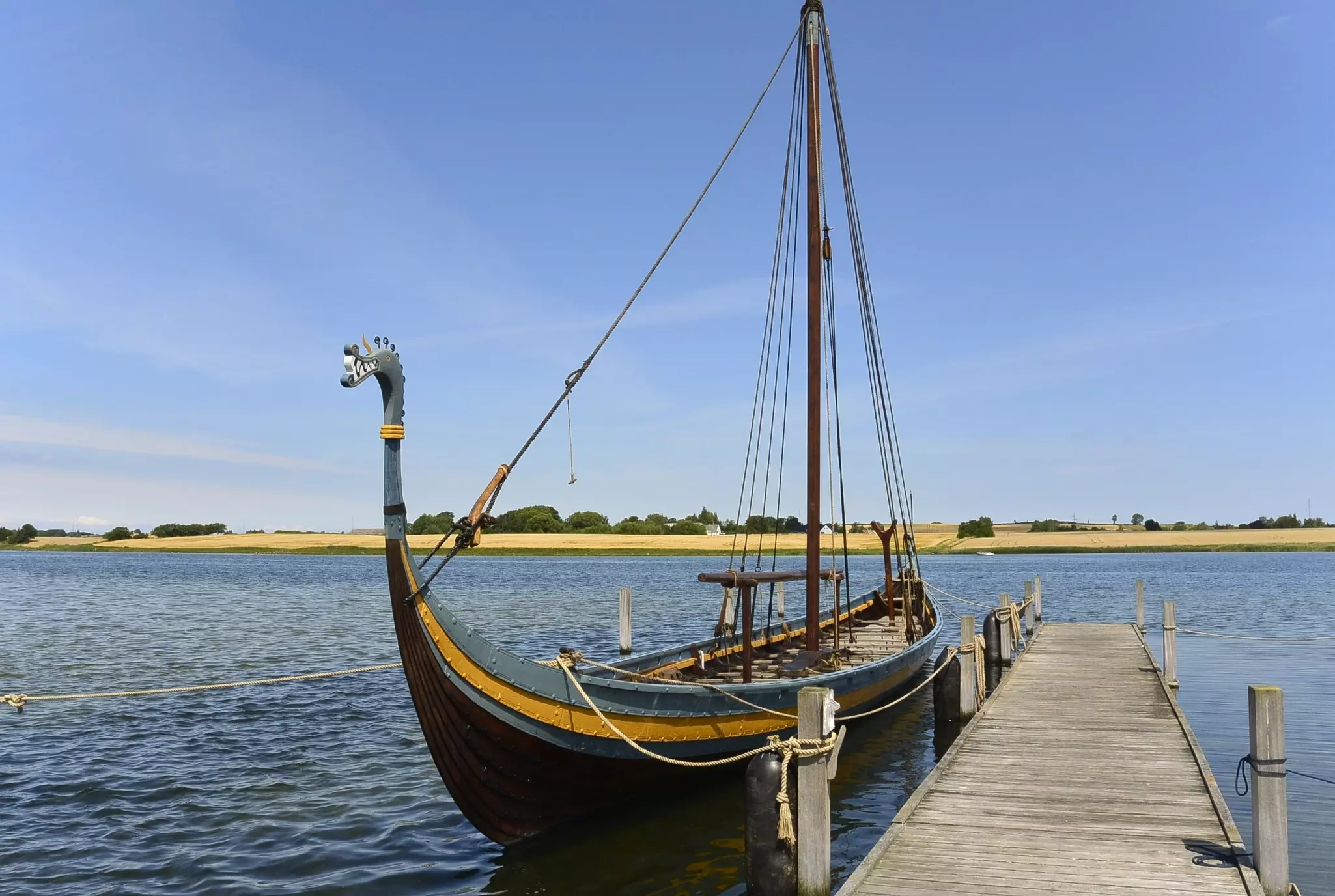 A reconstructed Viking shop with a dragon figurehead floats in the water next to a dock.