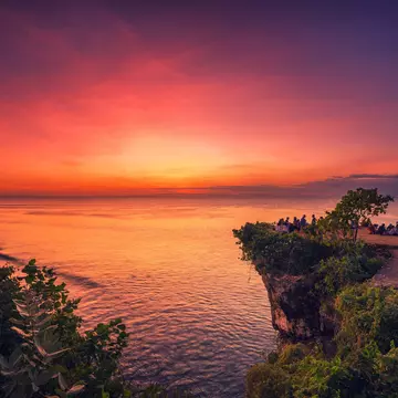 Bali, South Kuta, Badung - Indonesia - Mart 9, 2022: Travel people seating on the top mountain cliff on Balangan Beach and enjoy beautiful sunset. Bali, Indonesia