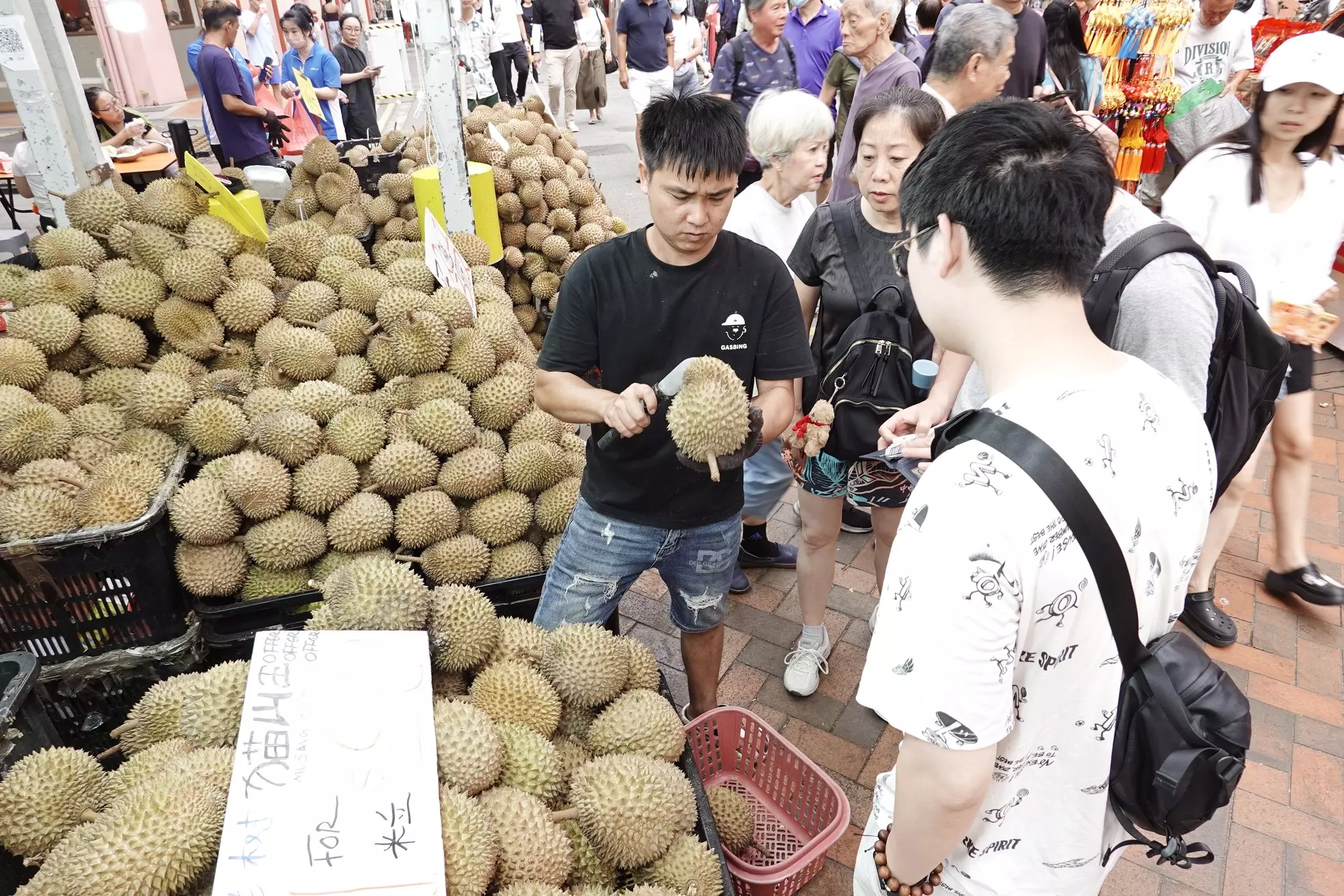 A vendor next pile of spiky fruits for sale at a street market, with customers passing by