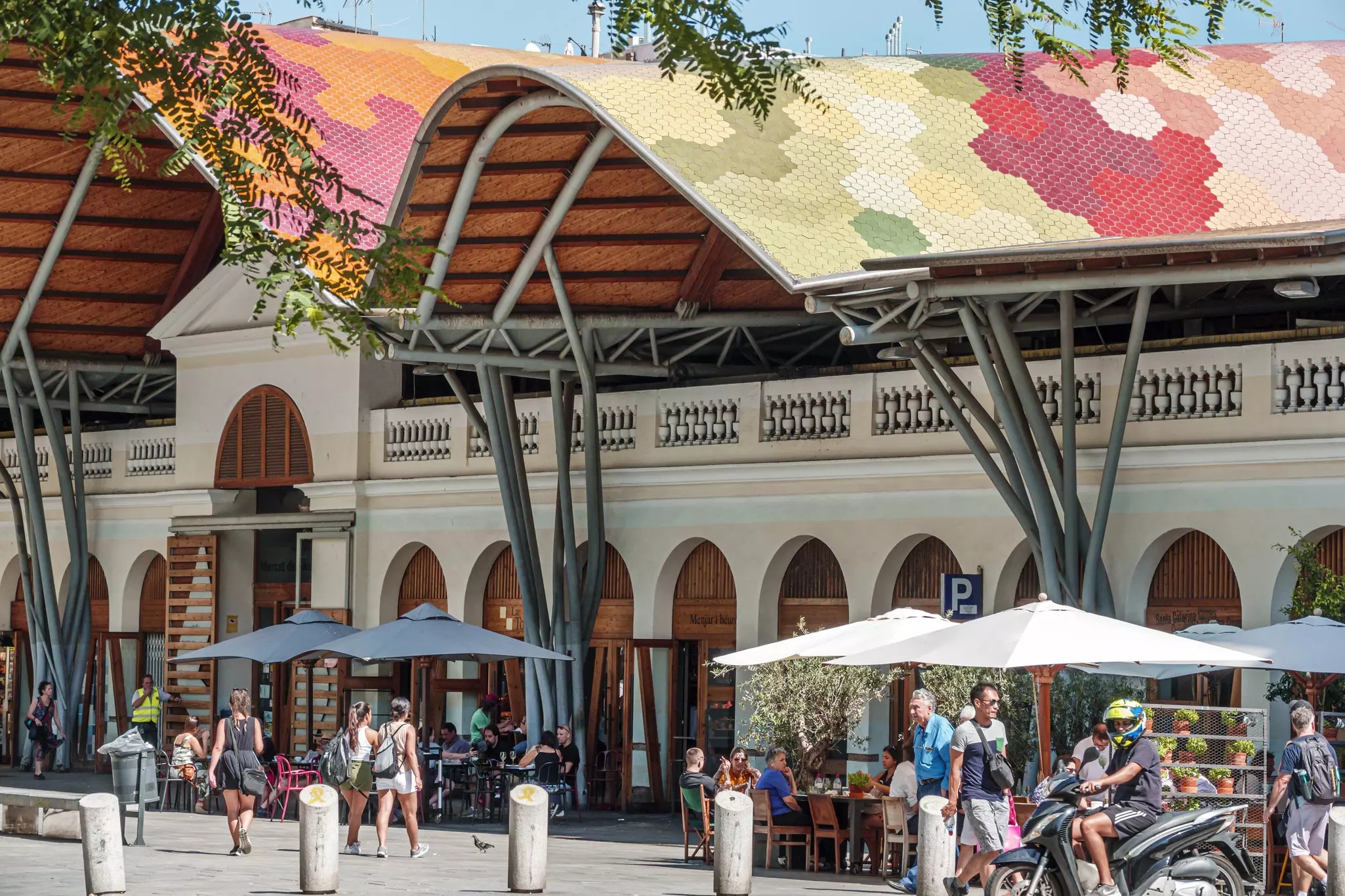 Exterior of a market with a colorful roof on a sunny day with customers dining at its terrace
