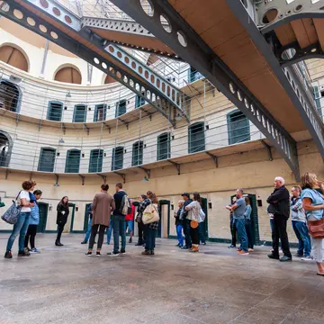 A tour group stands in the big hall of a prison building surrounded by doors to individual cells