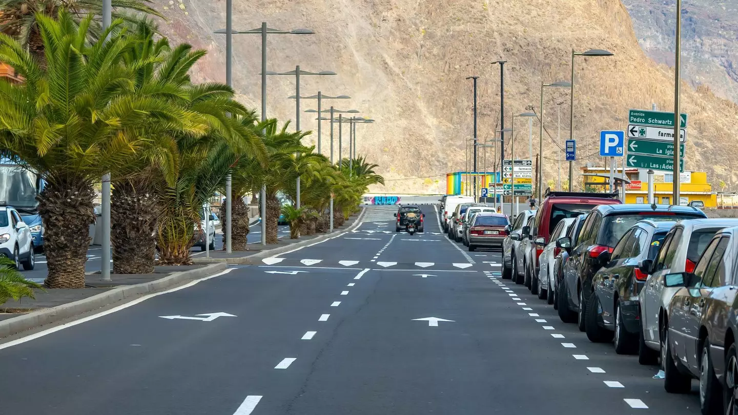 A jeep driving toward a mountain on a road lined with cars