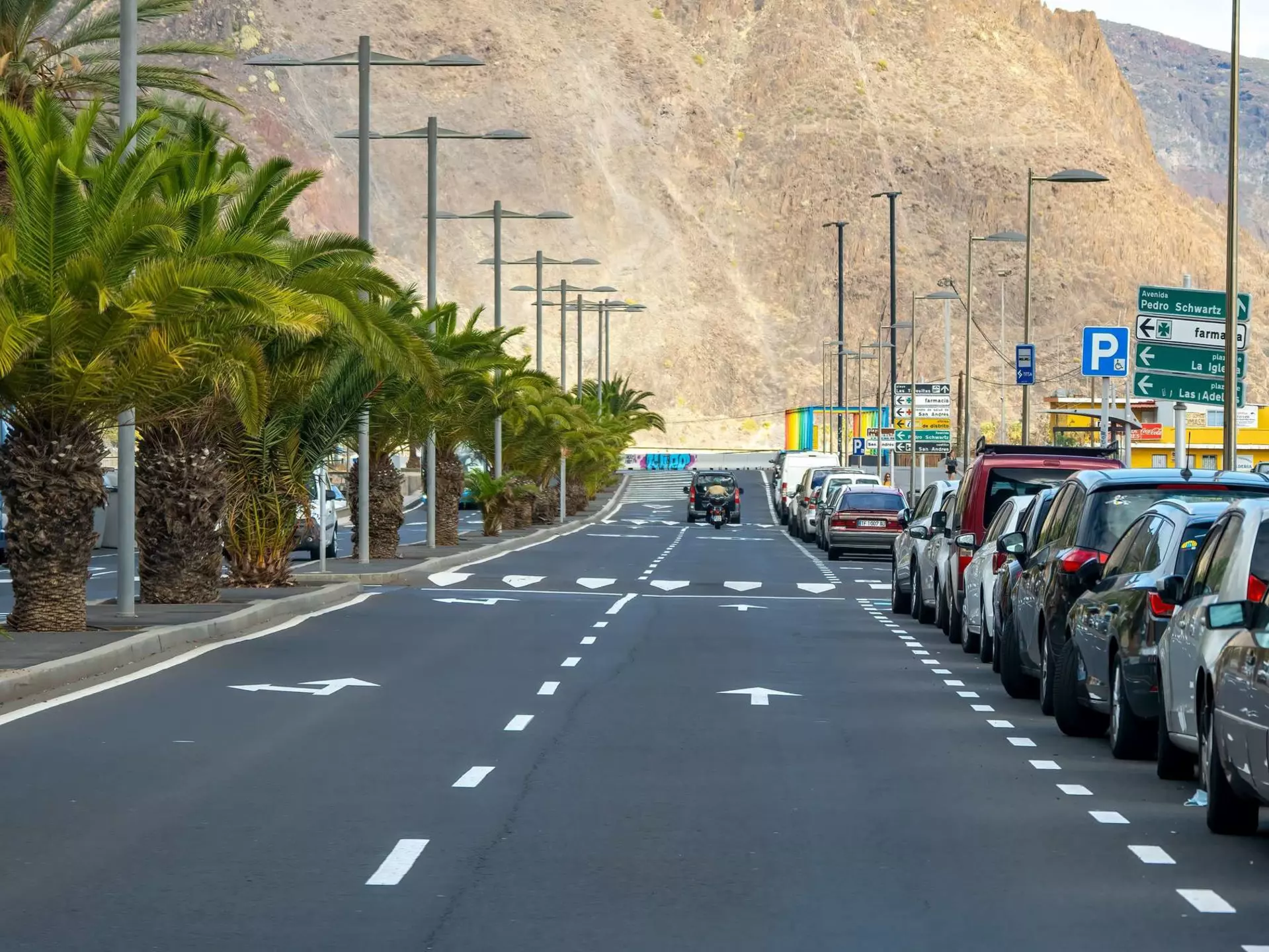 A jeep driving toward a mountain on a road lined with cars
