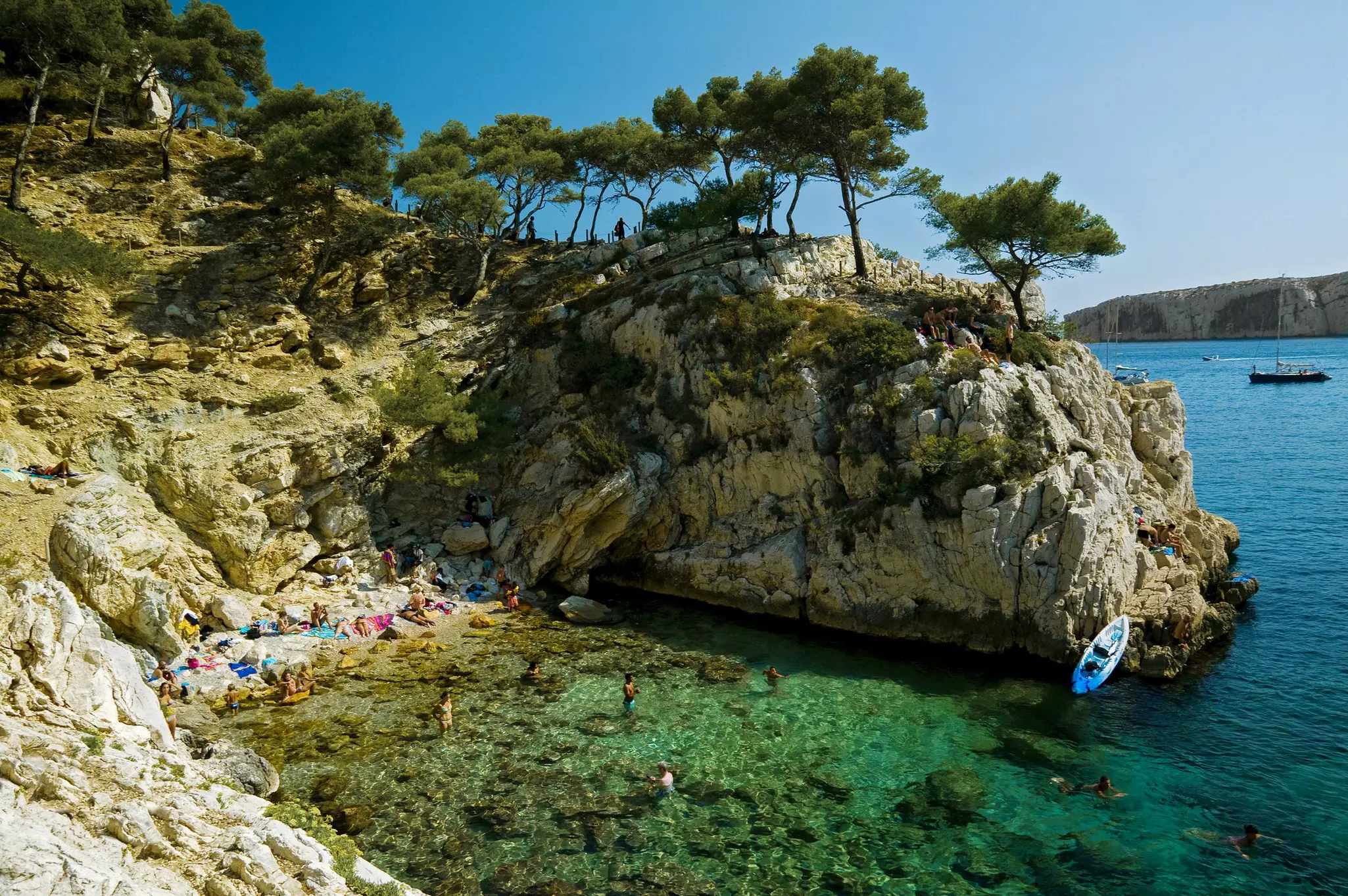 A small cove at the foot of rocky sea cliffs with people sunbathing and playing in the water