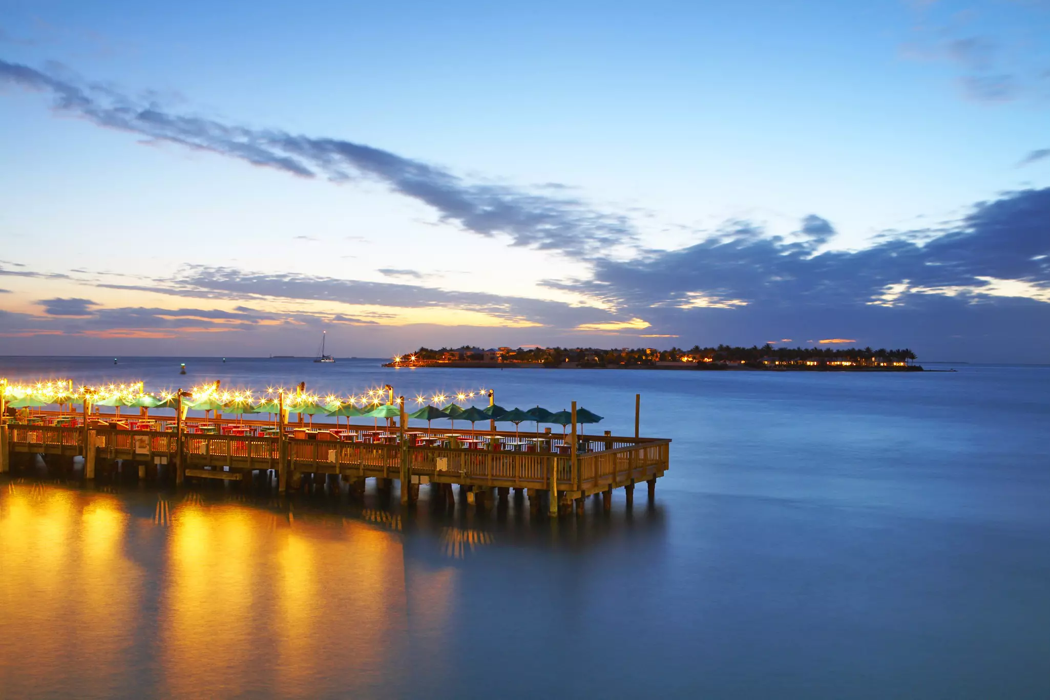 An aerial view of a pier jutting into the water by night, with lights all aglow, Key West