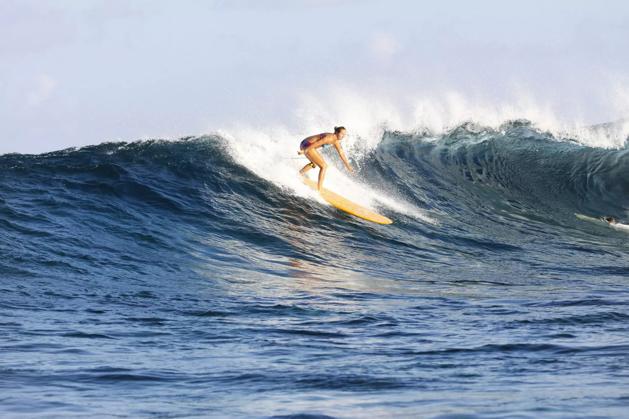 A surfer on a yellow board rides a crashing wave in the Maldives.