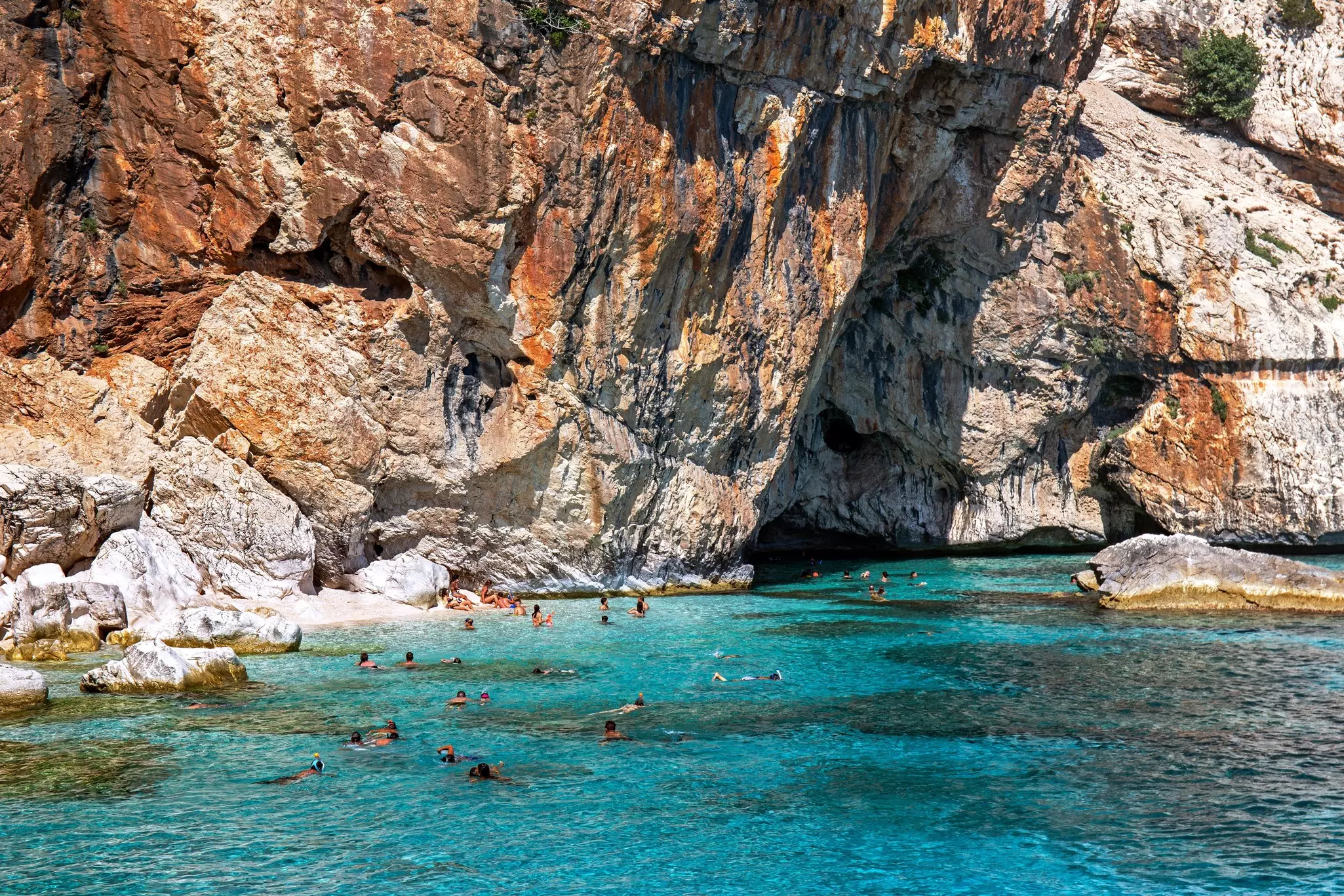 People swimming in the turquoise waters of Cala Mariolu, Sardinia, Italy.
