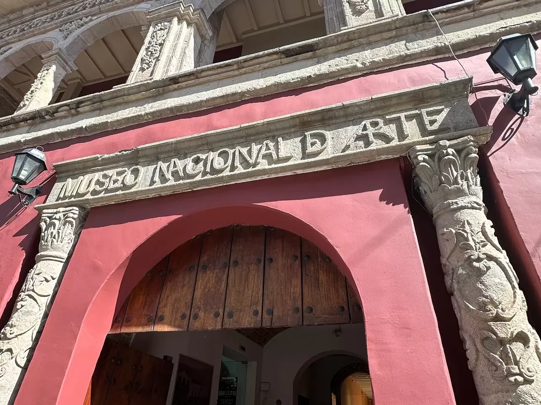 A carved stone doorway inscribed Museo Nacional de Arte set in a deep pink wall, flanked by ornate columns below an arcaded upper storey.