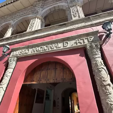 A carved stone doorway inscribed Museo Nacional de Arte set in a deep pink wall, flanked by ornate columns below an arcaded upper storey.