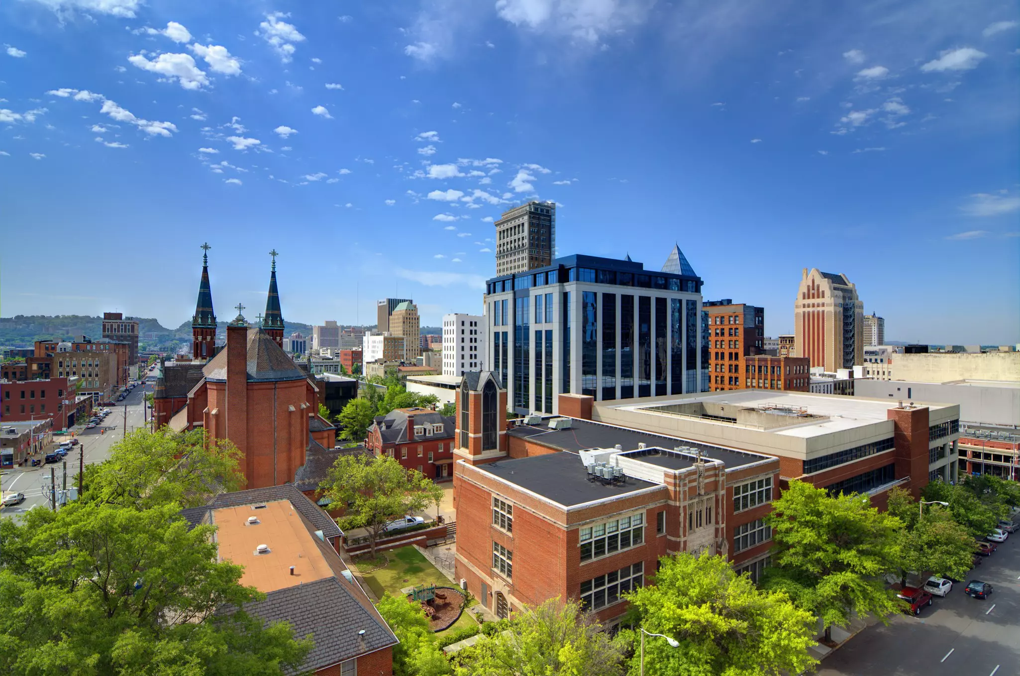 Red brick and modern glass city buildings under a blue, sunny sky.