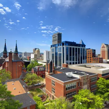 Red brick and modern glass city buildings under a blue, sunny sky.